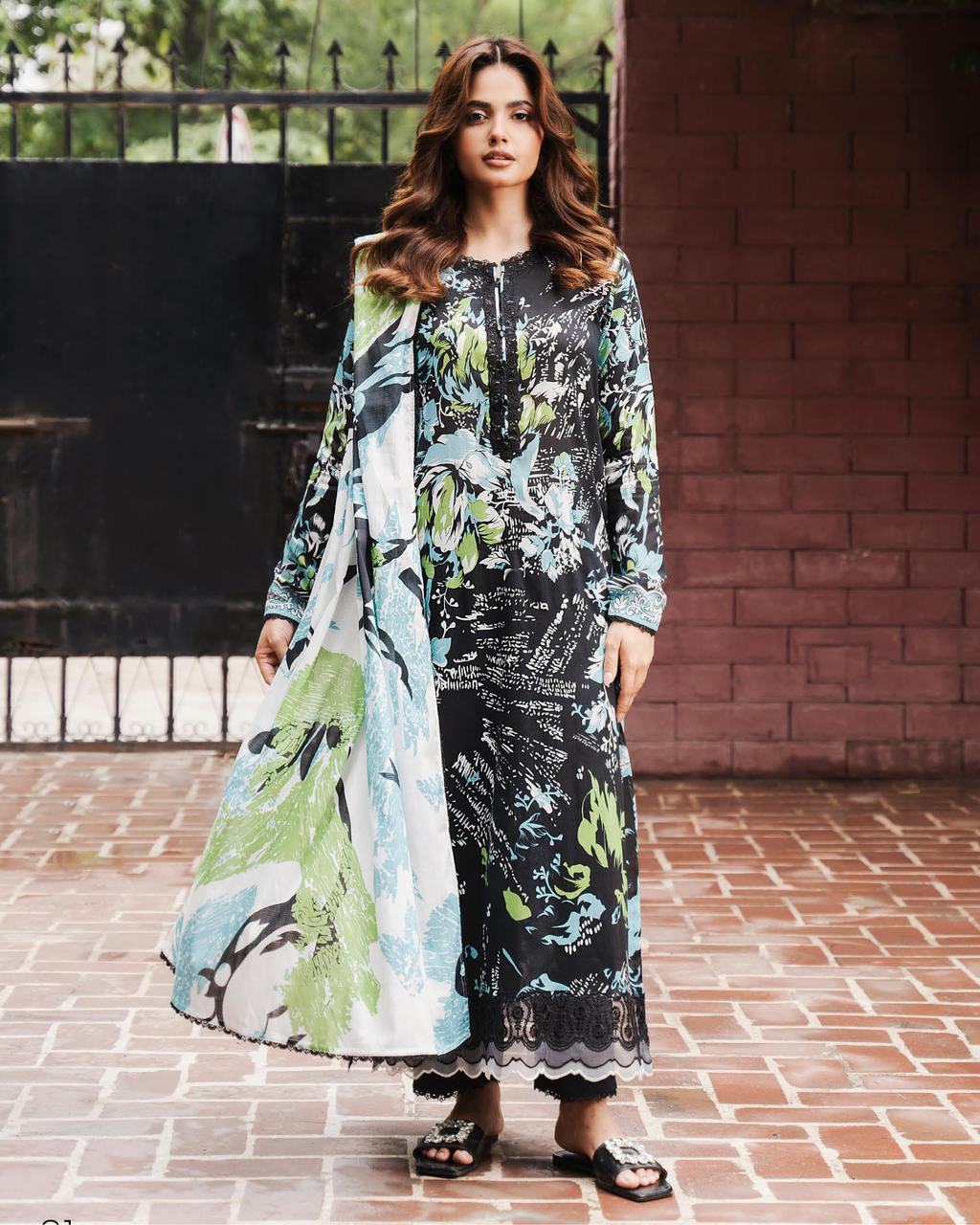 Woman wearing a long, floral-patterned dress standing on a brick pavement.