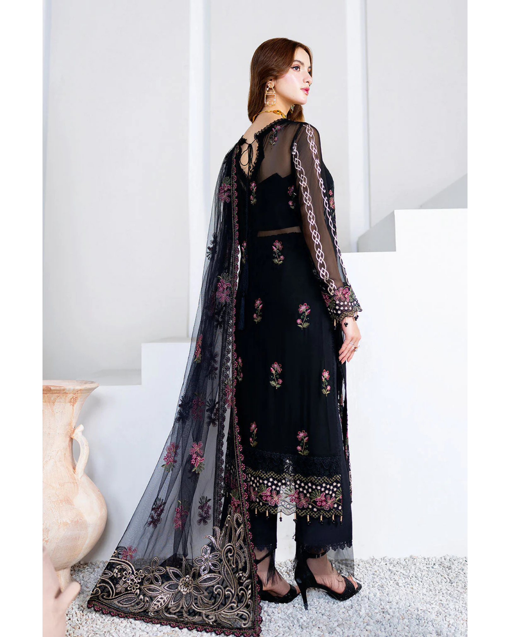 Woman wearing a black embroidered outfit with a sheer dupatta in a minimalistic setting