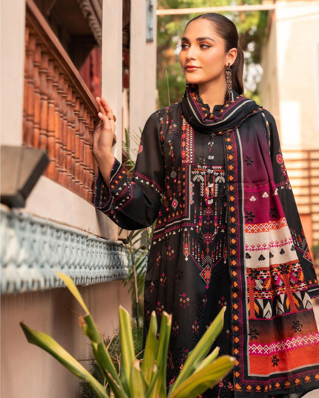 Woman wearing a black embroidered outfit with a colorful dupatta, standing outdoors.