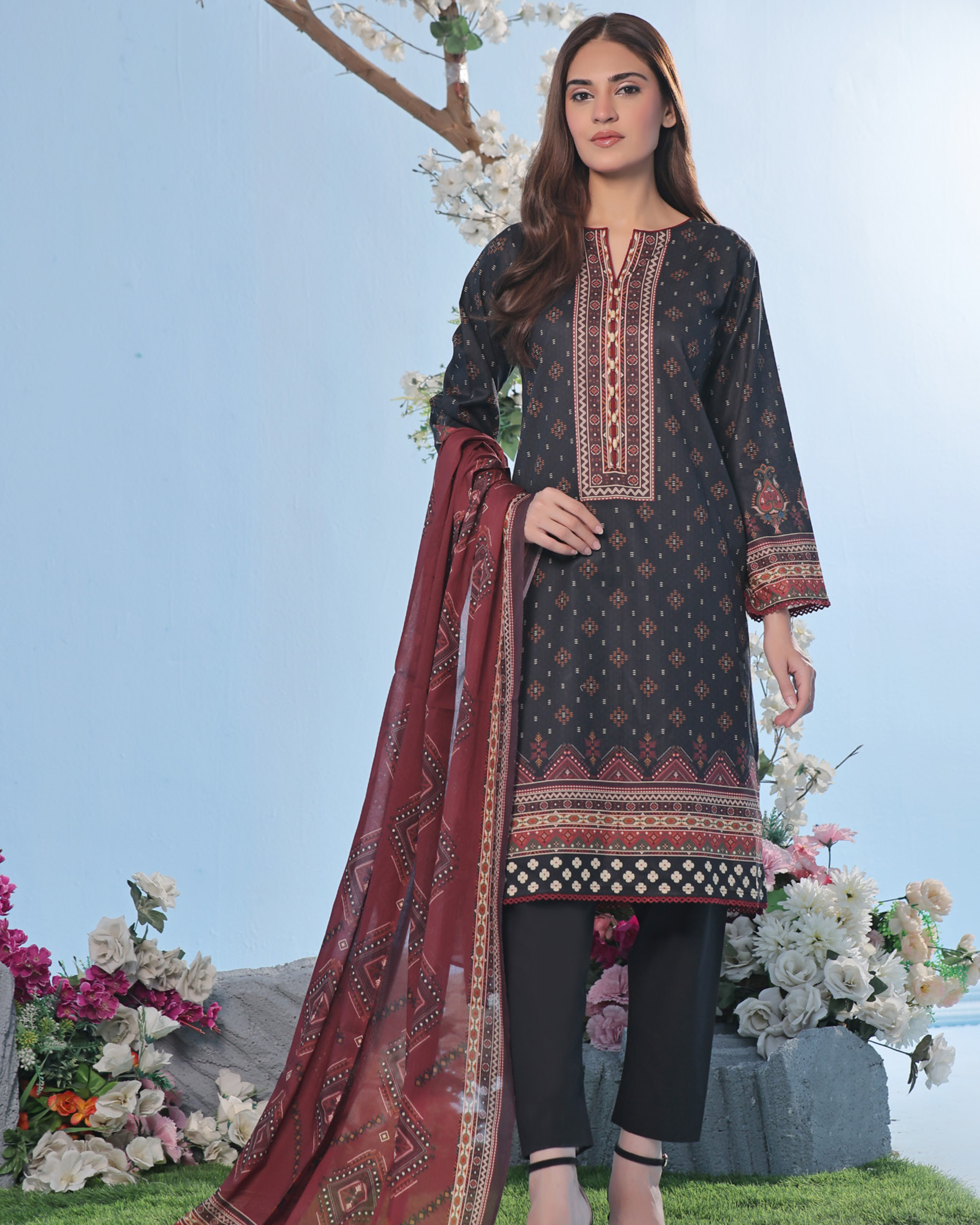 Woman wearing a black embroidered dress with a red dupatta in a garden setting