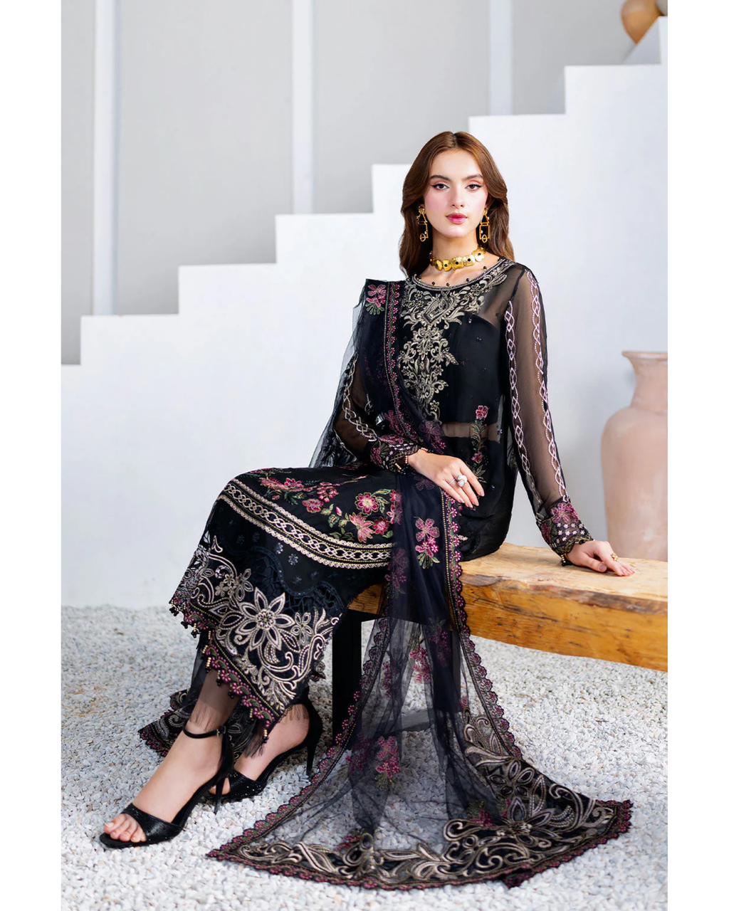 Woman in a black embroidered outfit sitting on a white staircase.