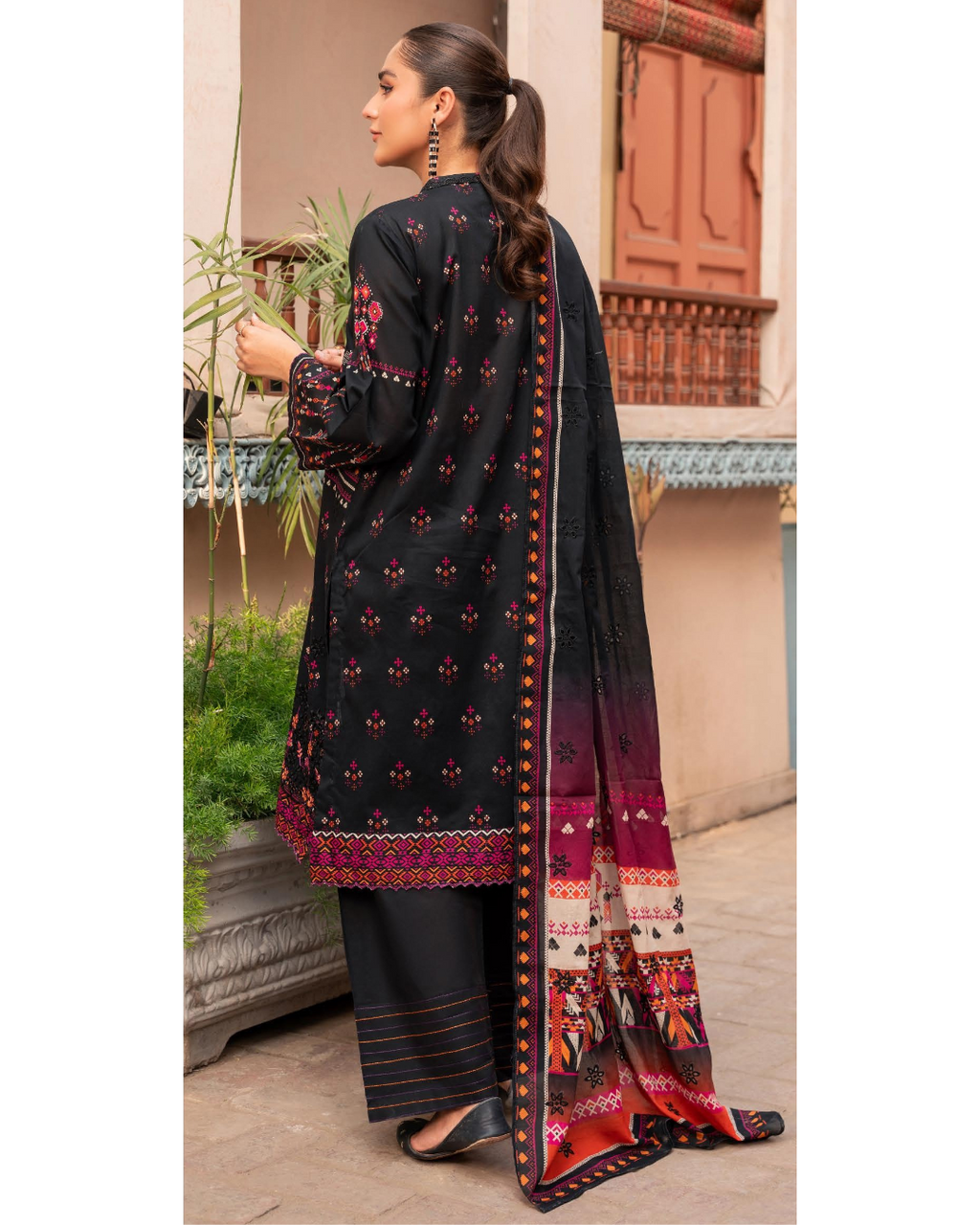 Woman wearing a black embroidered outfit with a colorful dupatta, standing outdoors.