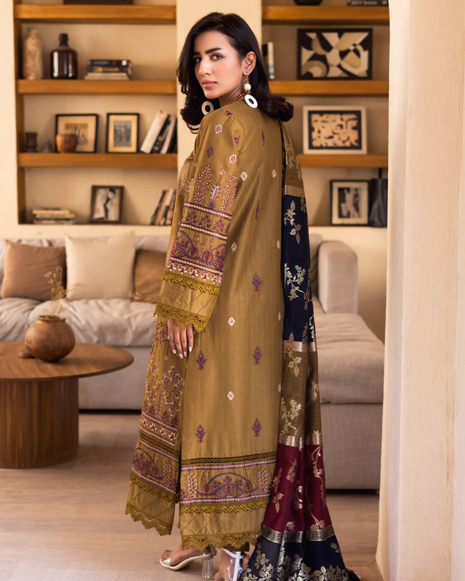 Woman in traditional embroidered outfit standing in a living room.