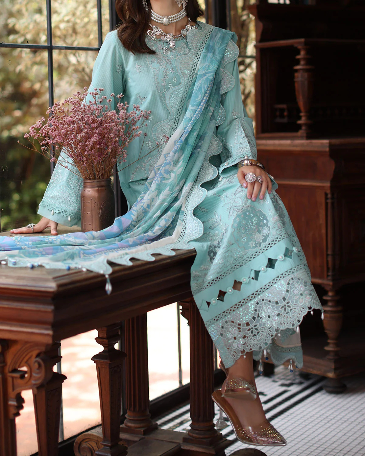 Woman in a light blue traditional outfit with a matching dupatta, sitting on a wooden bench.