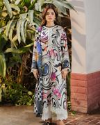 Woman wearing a colorful dress with abstract patterns standing in front of greenery.