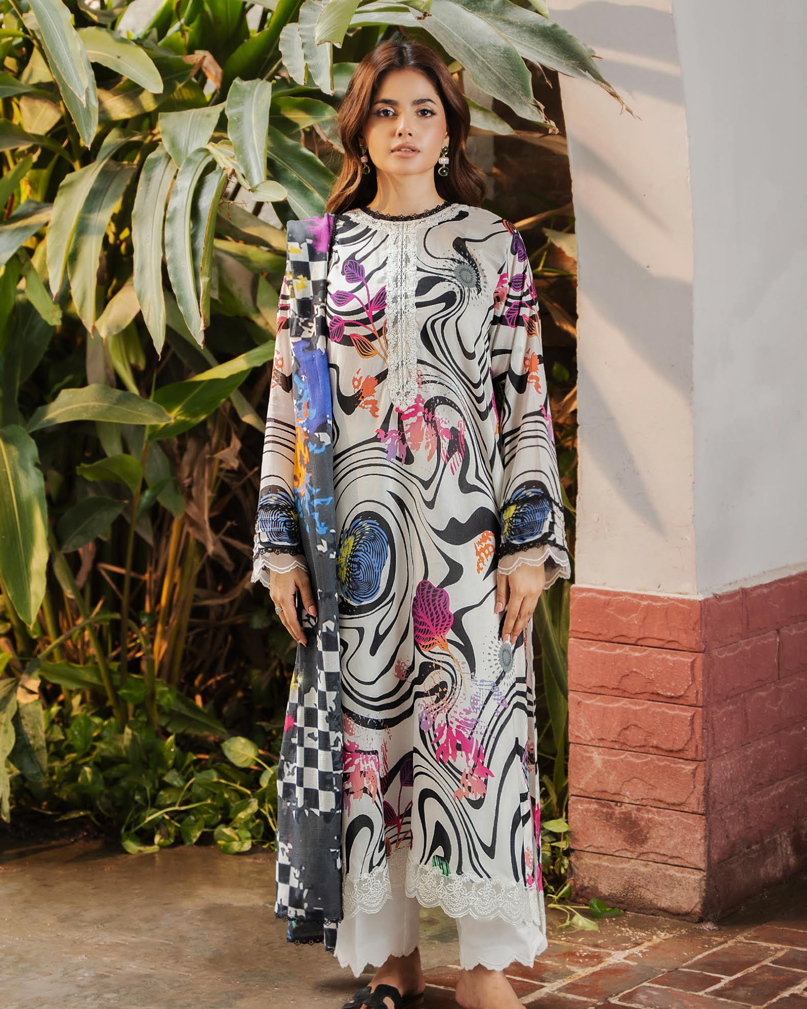 Woman wearing a colorful dress with abstract patterns standing in front of greenery.