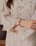 Person wearing a beige embroidered outfit with a close-up of hands wearing bracelets.