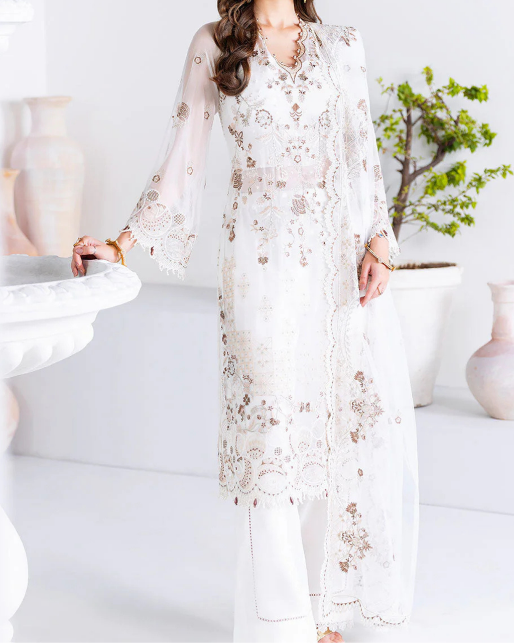 Woman wearing a white embroidered outfit in a minimalistic room.