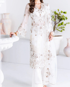 Woman wearing a white embroidered outfit in a minimalistic room.
