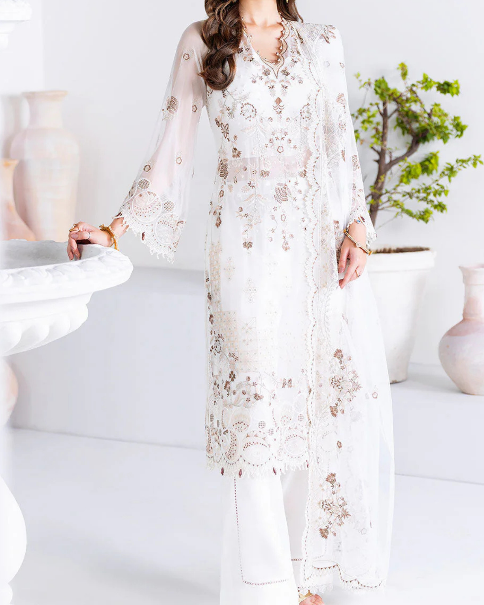 Woman wearing a white embroidered outfit in a minimalistic room.