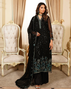 Woman in a black embroidered outfit standing in an elegant room with ornate chairs and curtains.