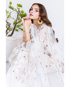 Woman wearing a white embroidered dress with gold jewelry against a white background