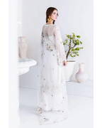 Woman wearing a white embroidered dress in a minimalistic setting with white walls and decorative elements.