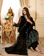 Woman in a black embroidered saree sitting in an elegant room with gold decor.