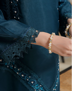 Person wearing a dark blue embroidered garment with a bracelet on a blurred background