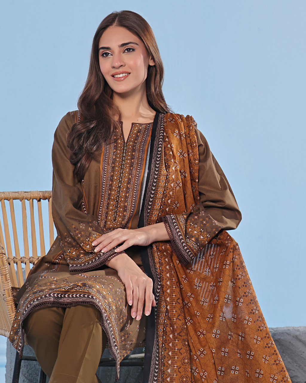 Woman wearing a brown traditional outfit with intricate patterns on a light blue background