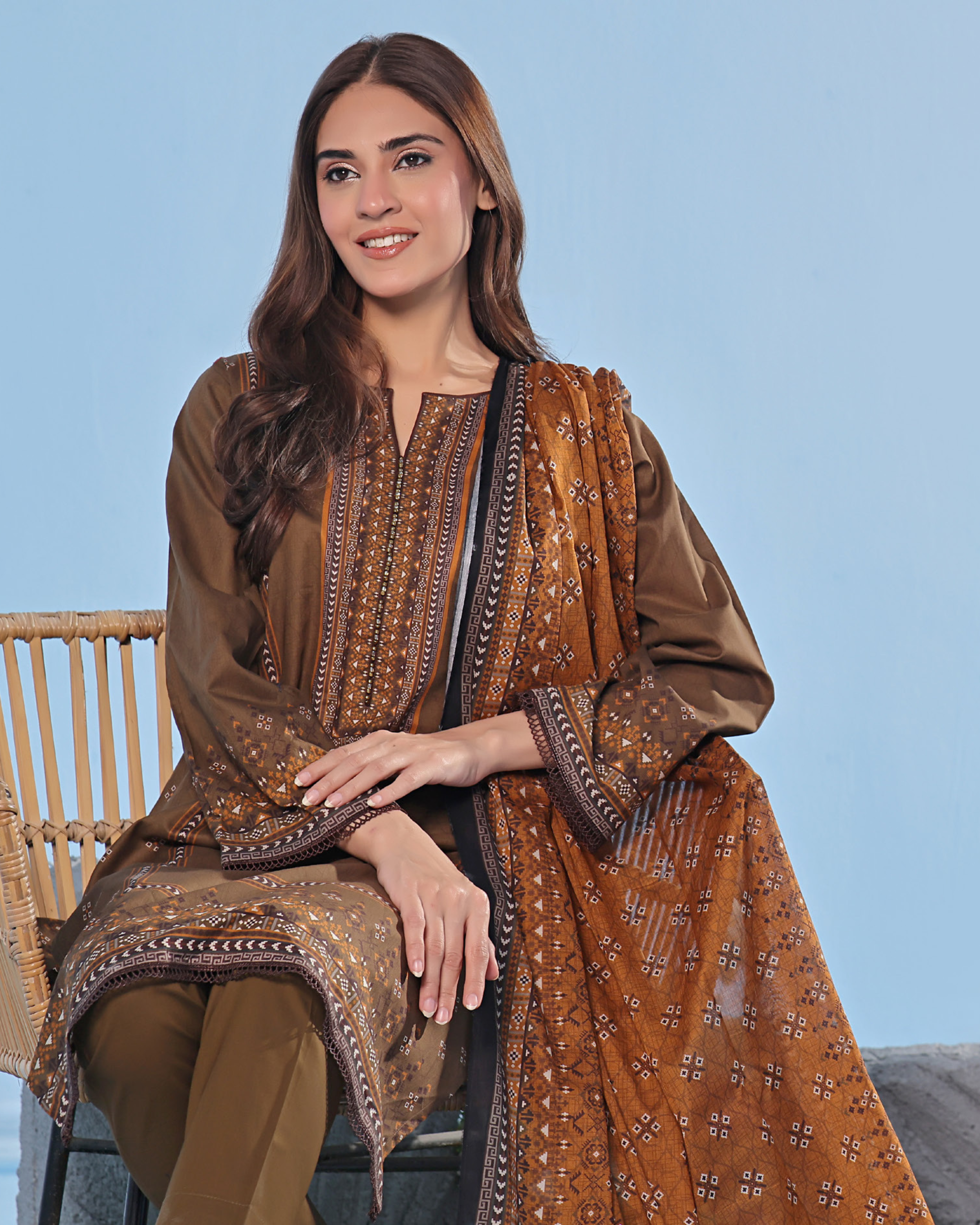 Woman wearing a brown traditional outfit with intricate patterns on a light blue background