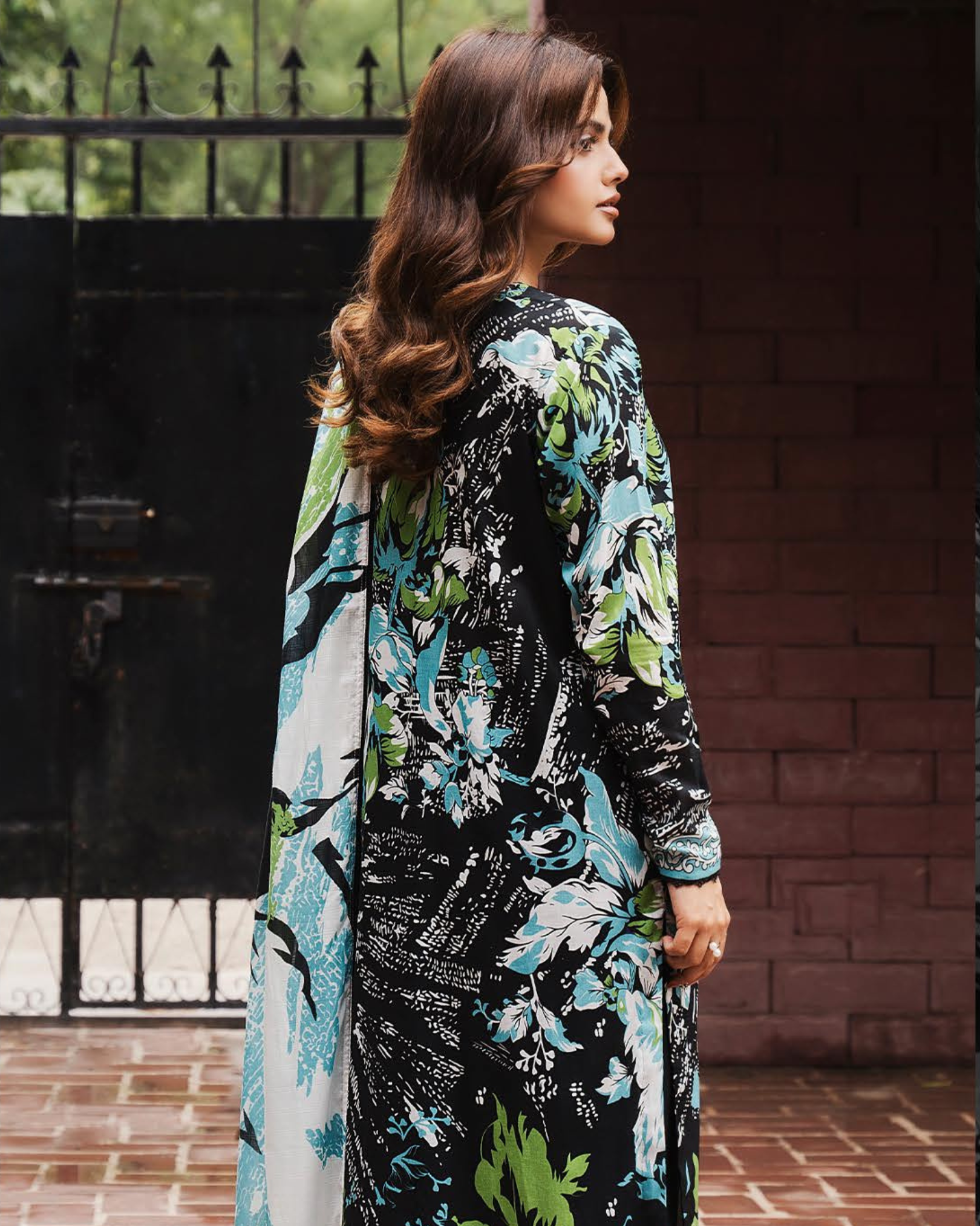 Woman wearing a floral dress with a matching scarf in front of a brick wall.