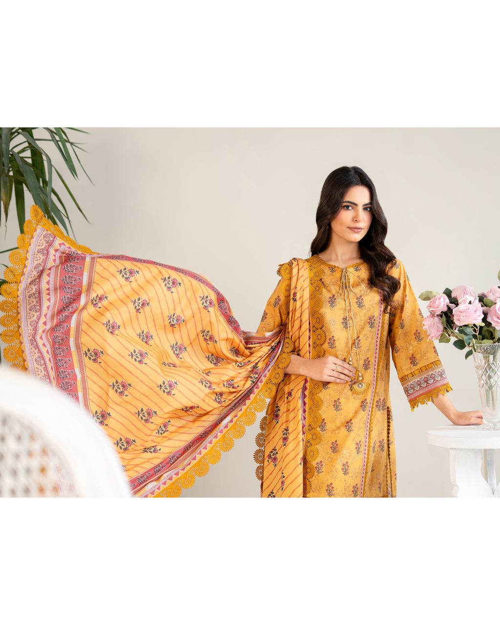 Woman wearing a yellow traditional outfit with a patterned dupatta in a minimalistic setting.