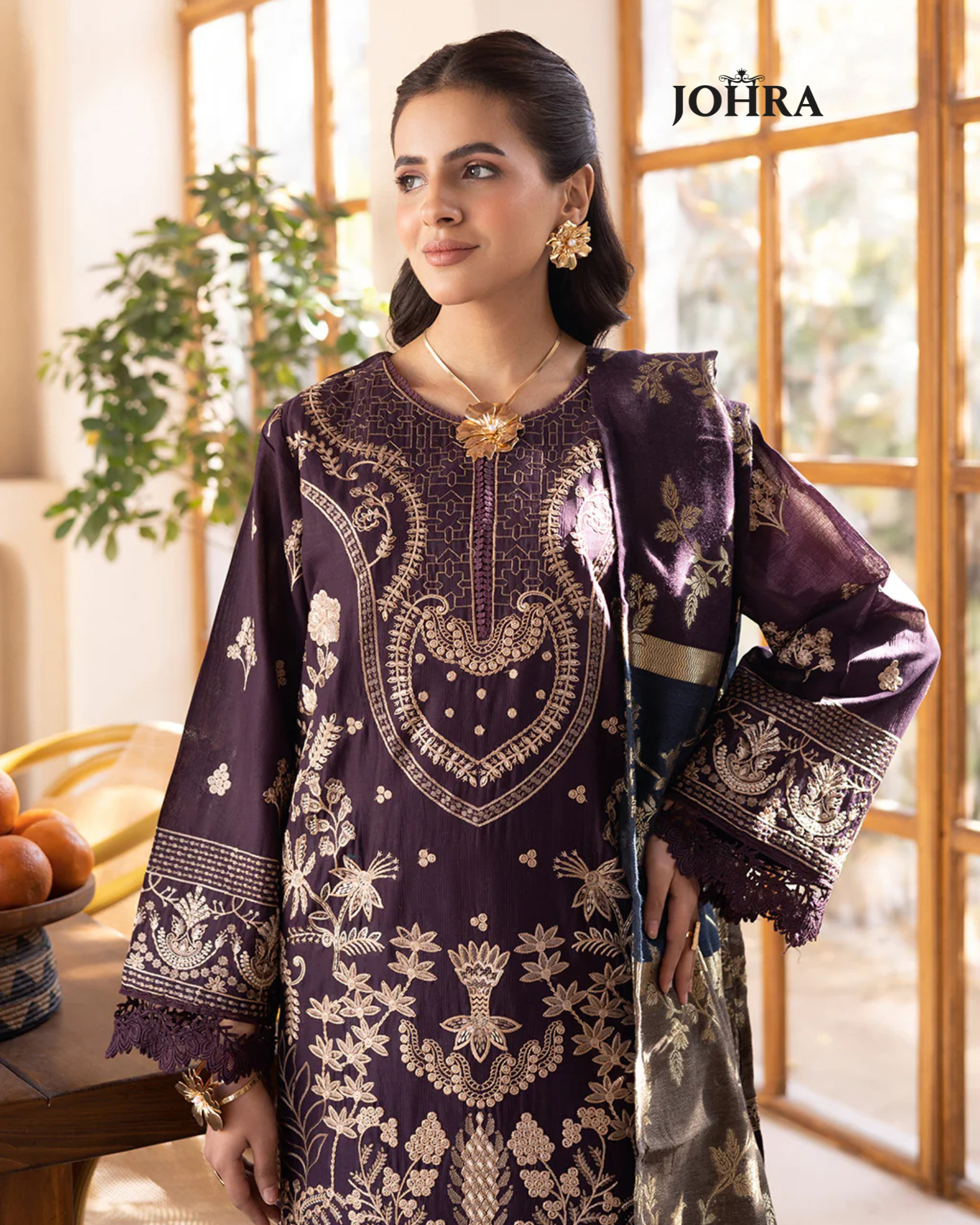 Woman wearing a purple embroidered traditional outfit with 'JOHRA' branding.