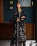 Woman wearing a black embroidered dress in an indoor setting with wooden furniture and decorative elements.