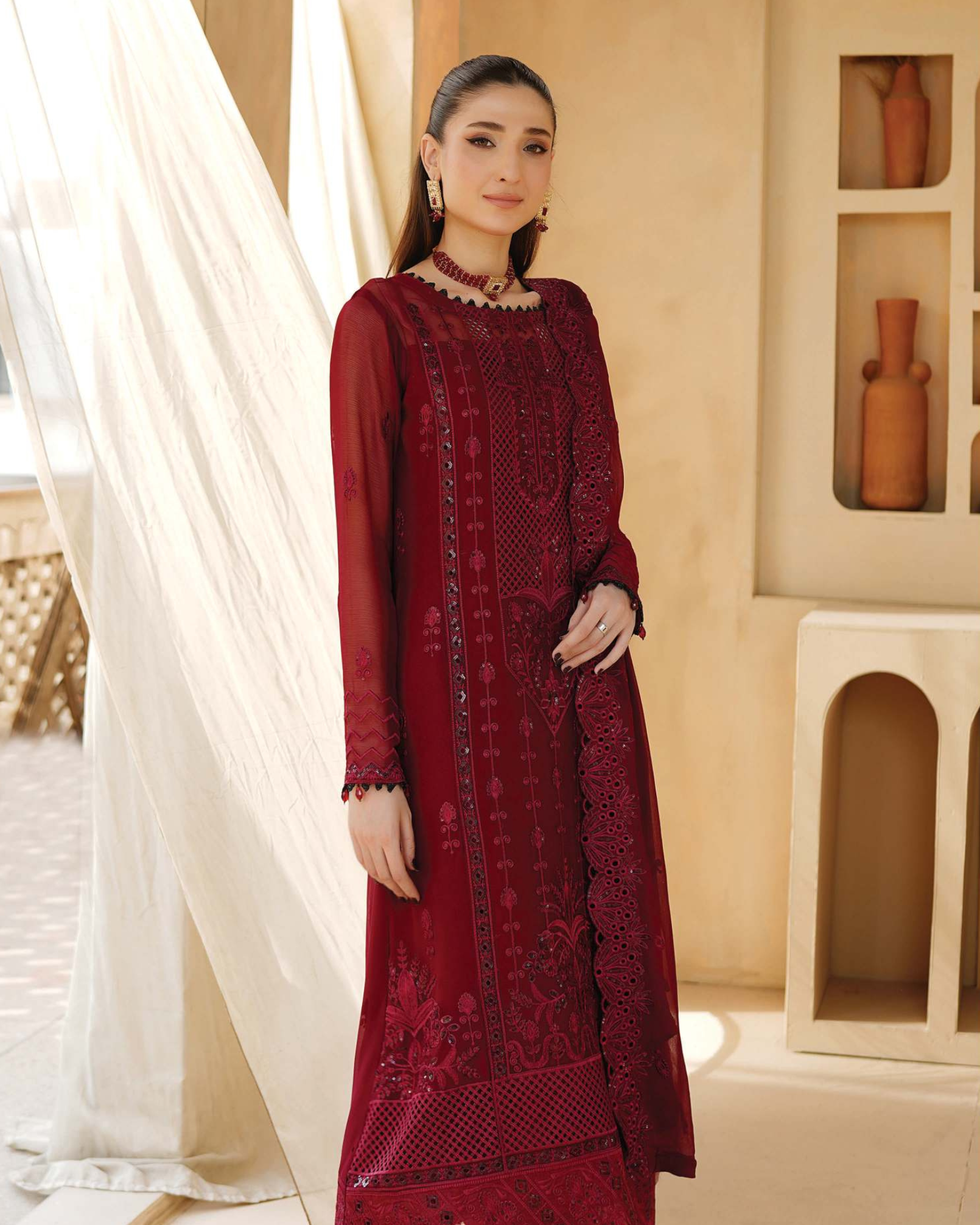 Woman wearing a red embroidered dress in a decorated room.