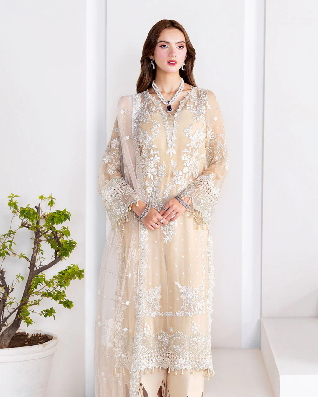 Woman wearing a beige embroidered outfit with a white background