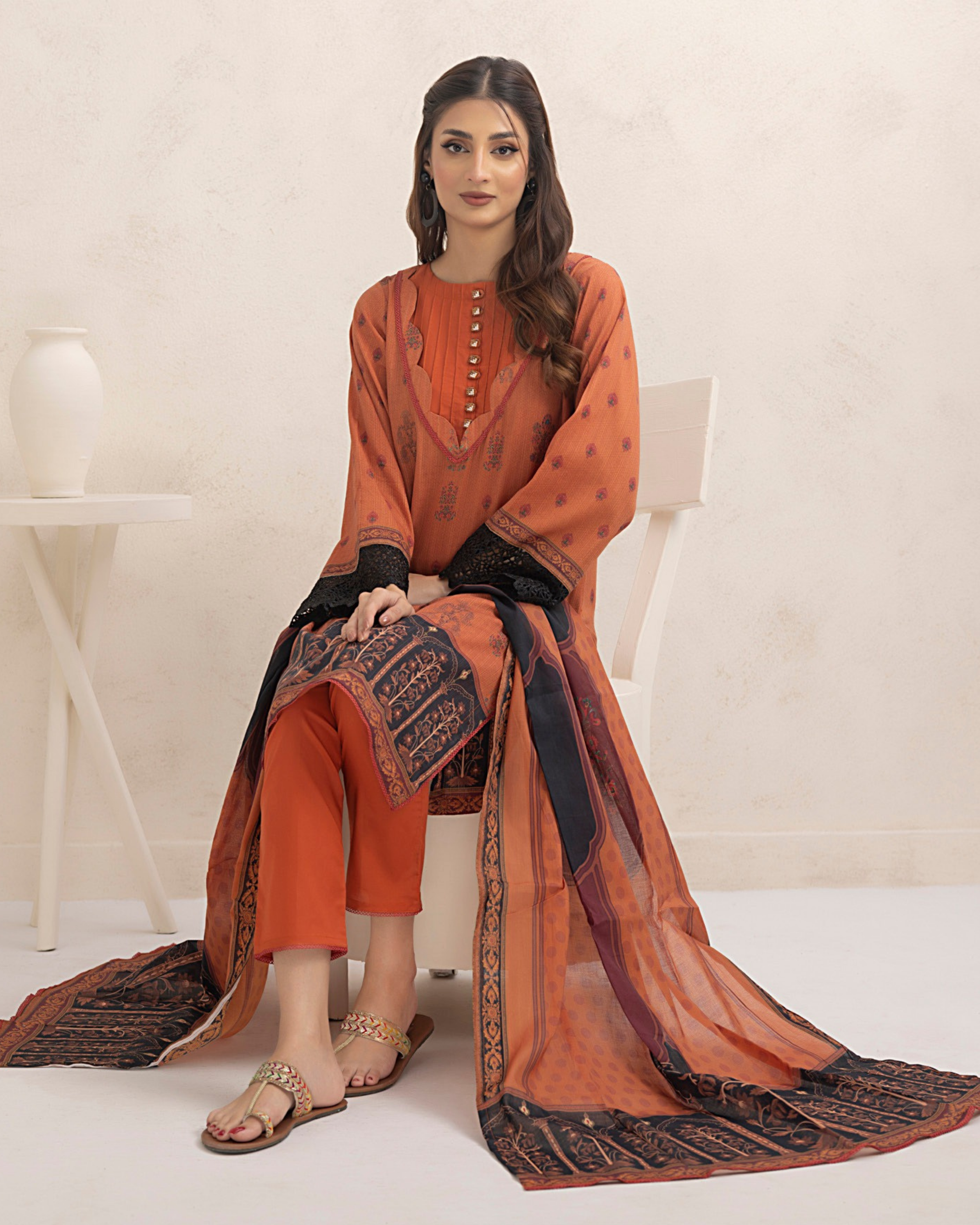 Woman wearing an orange traditional outfit with a black and gold scarf on a white background