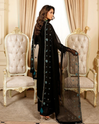 Woman in a black traditional outfit with floral patterns standing between two ornate chairs.