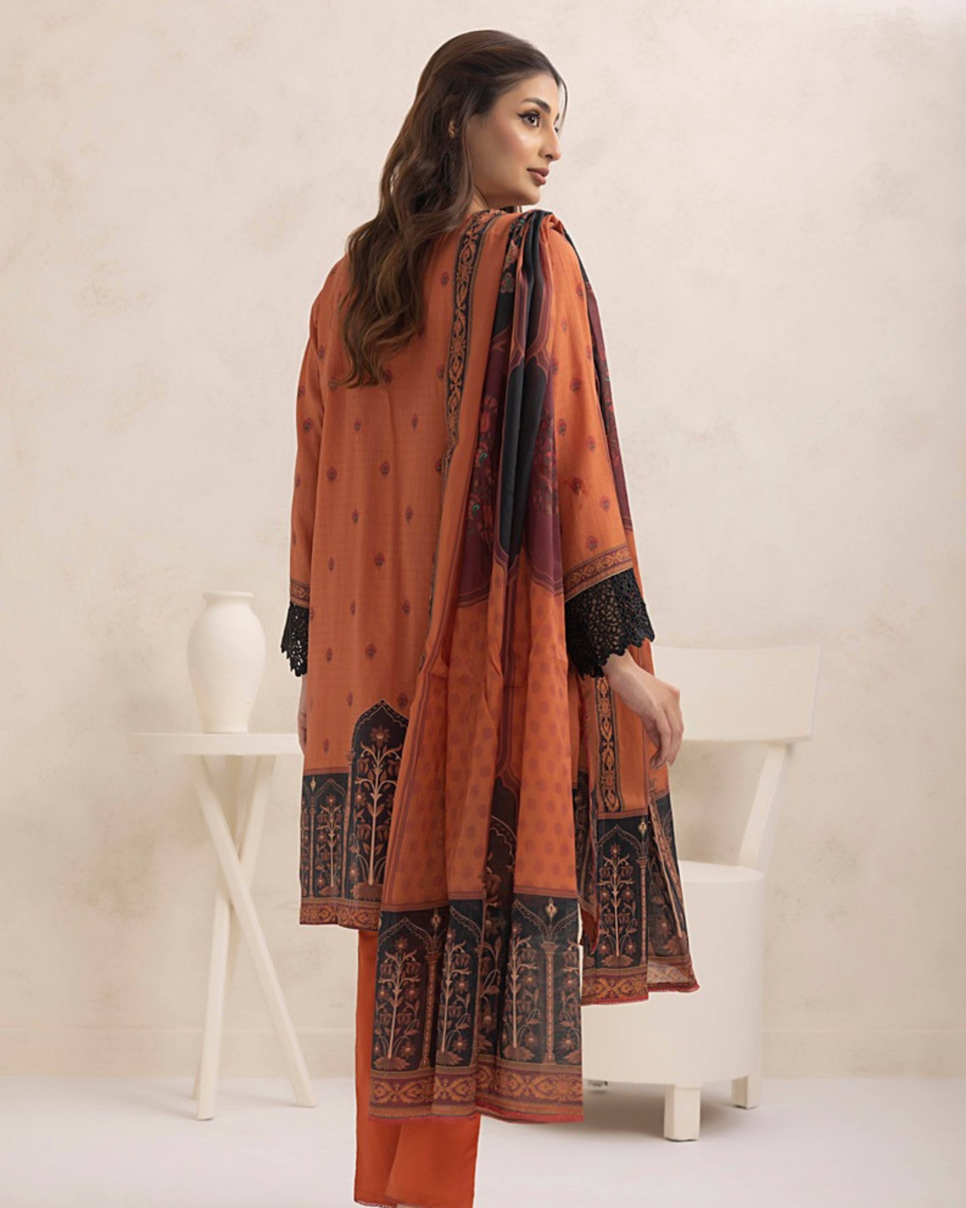 Woman wearing an orange traditional outfit with black patterns in a minimalistic setting.