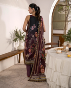 Woman in a dark purple embroidered traditional outfit standing in a room with a table and decor.