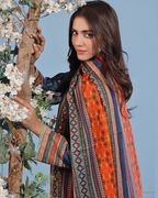 Woman wearing a colorful traditional outfit with a patterned shawl, holding flowers against a blue sky.