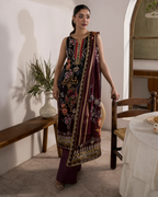 Woman in a traditional embroidered outfit standing in a room with a wooden bench and table.