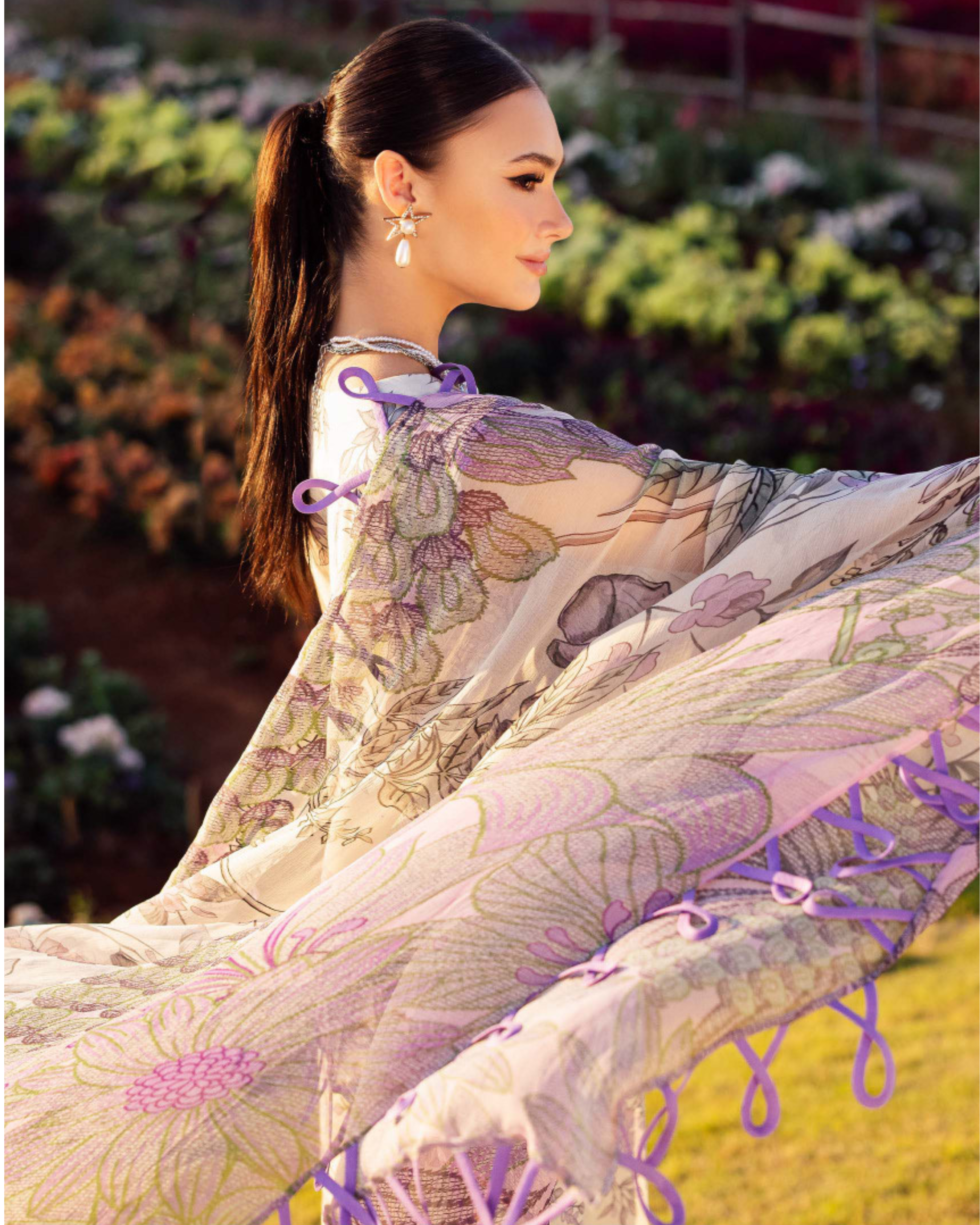 Woman in a floral dress with purple accents standing outdoors with plants in the background