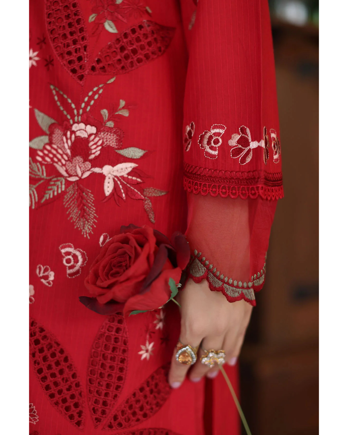 Red embroidered dress with floral patterns and a hand holding a red rose.