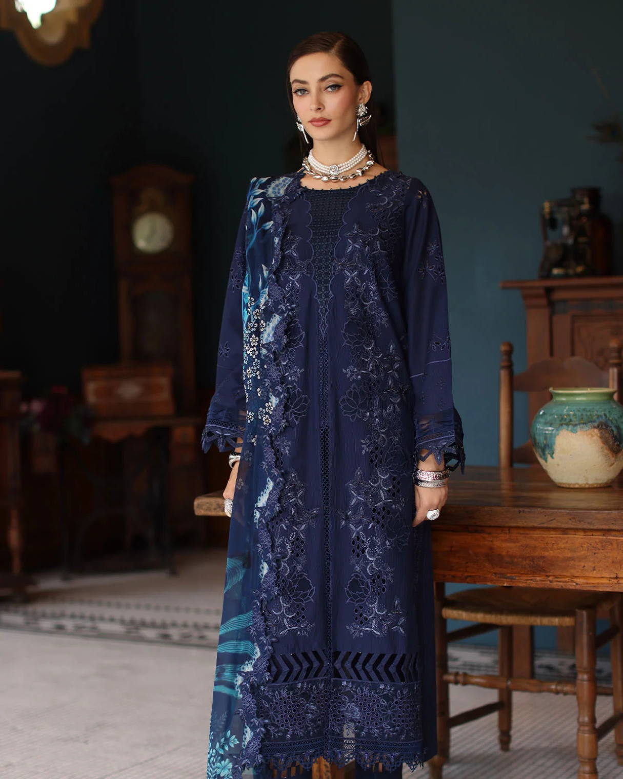 Woman wearing a dark blue embroidered dress in an indoor setting with wooden furniture.