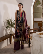 Woman in traditional embroidered outfit standing in a room with a table and plant.