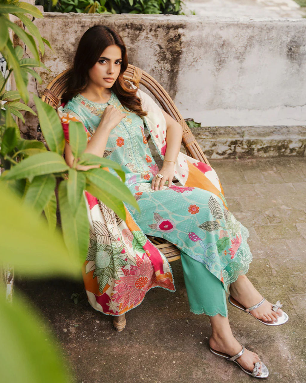 Woman in a colorful floral dress sitting on a wicker chair outdoors.