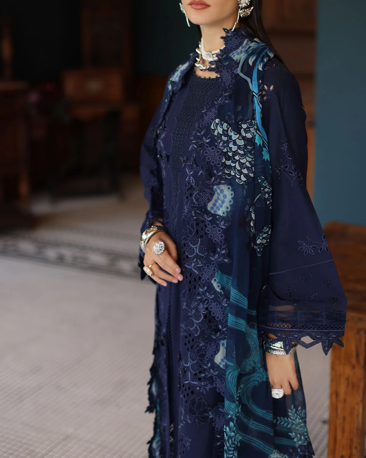 Woman wearing a dark blue embroidered outfit with a matching shawl indoors.