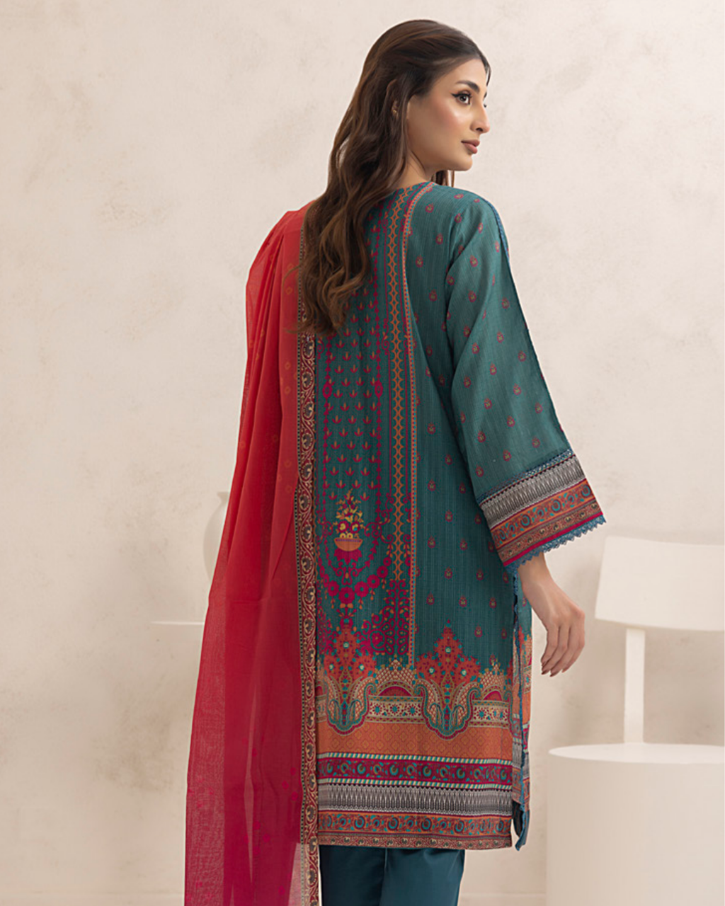 Woman wearing a teal embroidered dress with a red dupatta on a beige background