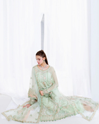 Woman in a light green traditional outfit sitting on a white surface with a white background