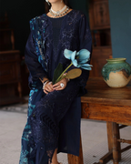 Woman in a dark blue lace dress holding flowers, sitting on a wooden stool.