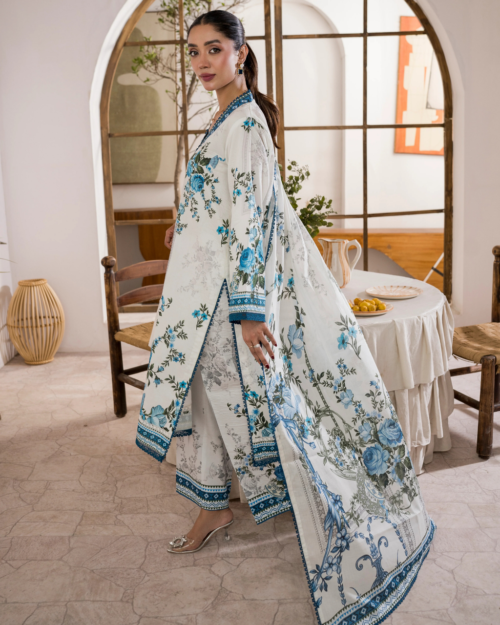 Woman wearing a floral outfit in a room with wooden furniture and a mirror.