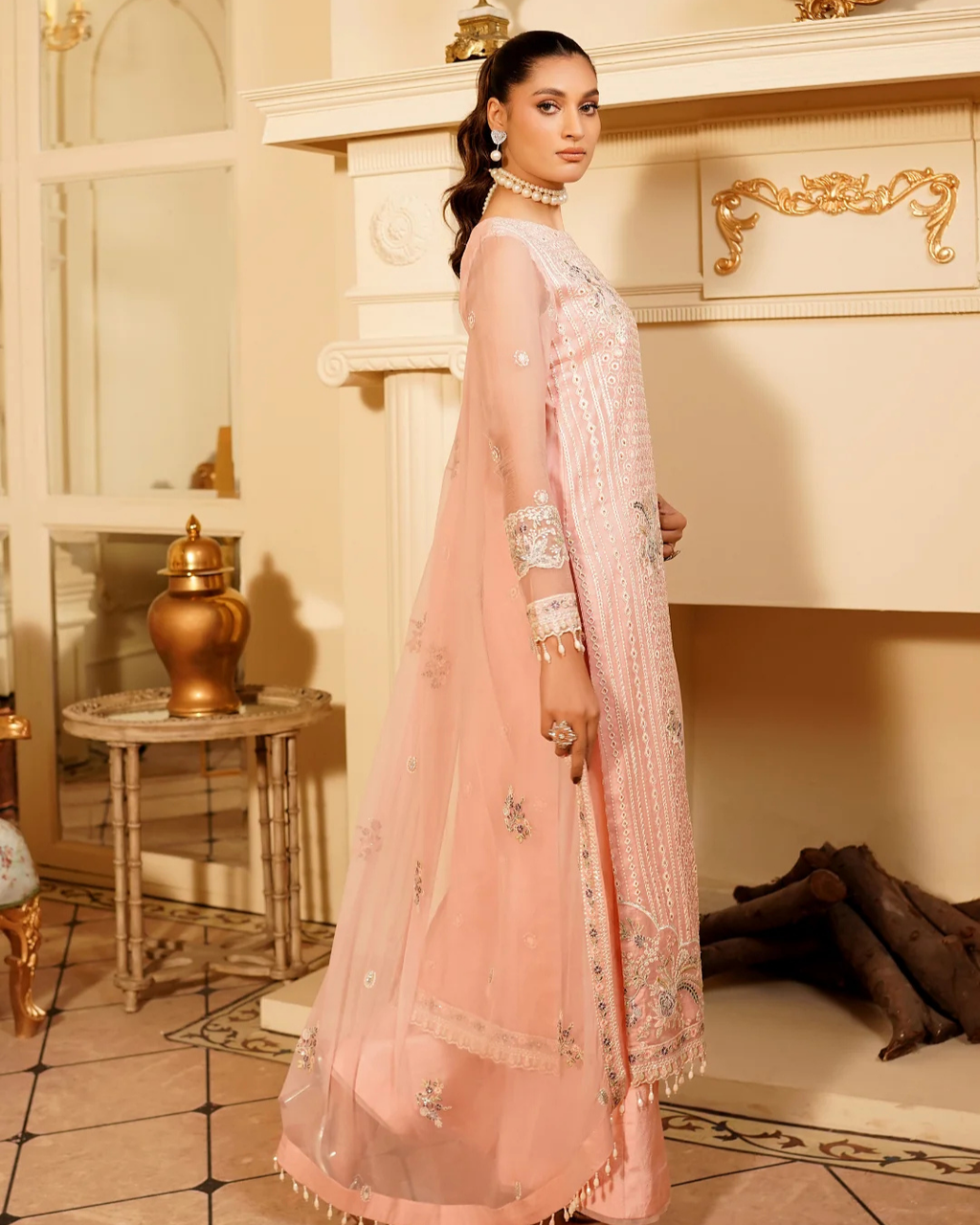 Woman in a light pink traditional outfit standing in an elegant room with decorative elements.