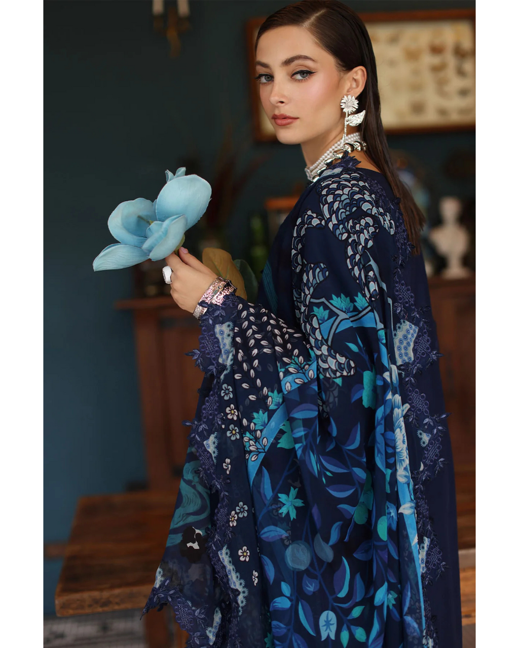 Woman in a blue floral dress holding a blue flower-like object indoors.