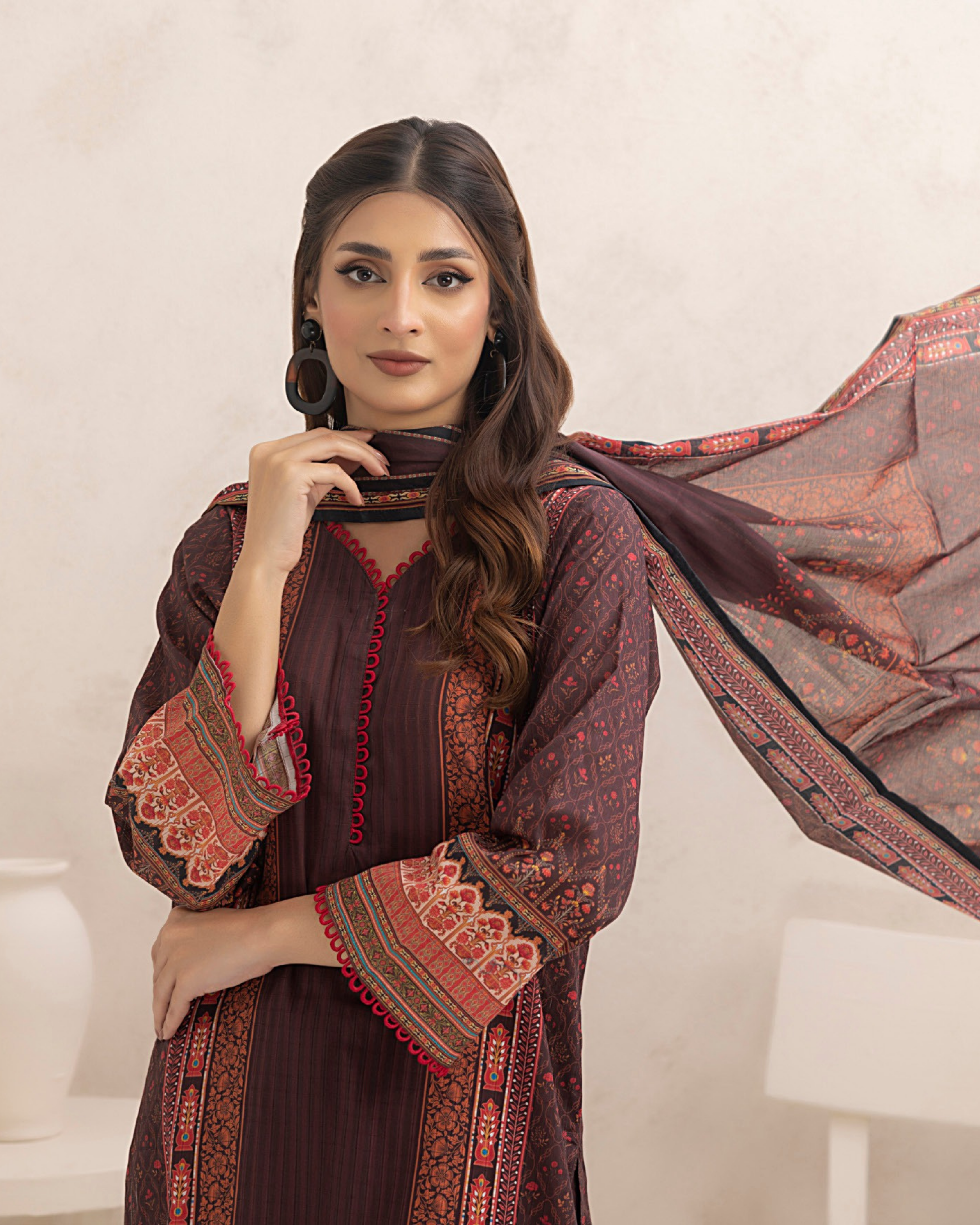 Woman wearing a dark brown dress with red and gold patterns, holding a matching dupatta.