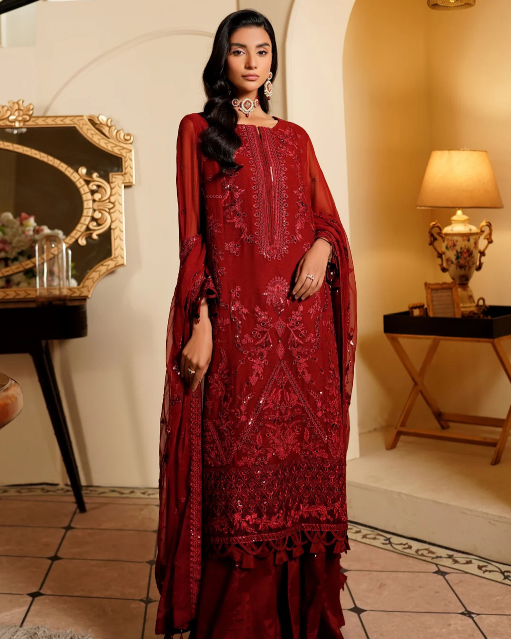 Woman in a red embroidered traditional outfit standing in an elegant room.