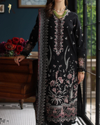 Woman wearing a black embroidered dress with floral patterns indoors.