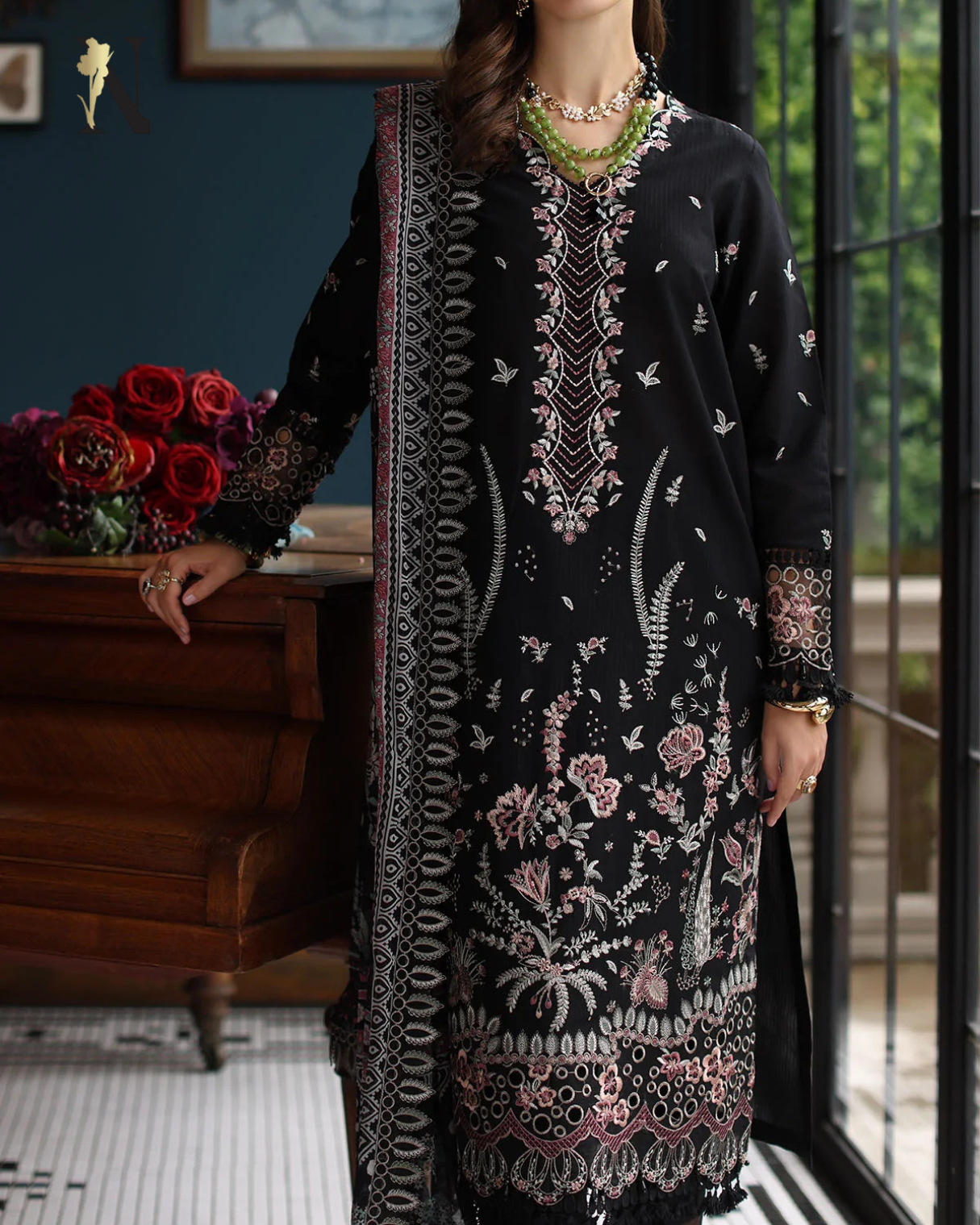 Woman wearing a black embroidered dress with floral patterns indoors.
