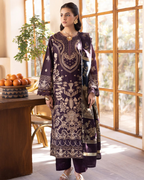 Woman in a dark purple embroidered outfit standing in a bright room with large windows.